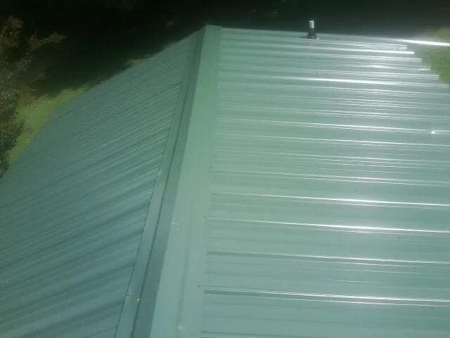 New green metal panels meeting at the ridge of a roof — Flat Roof Repair work by our crew in Carpenter