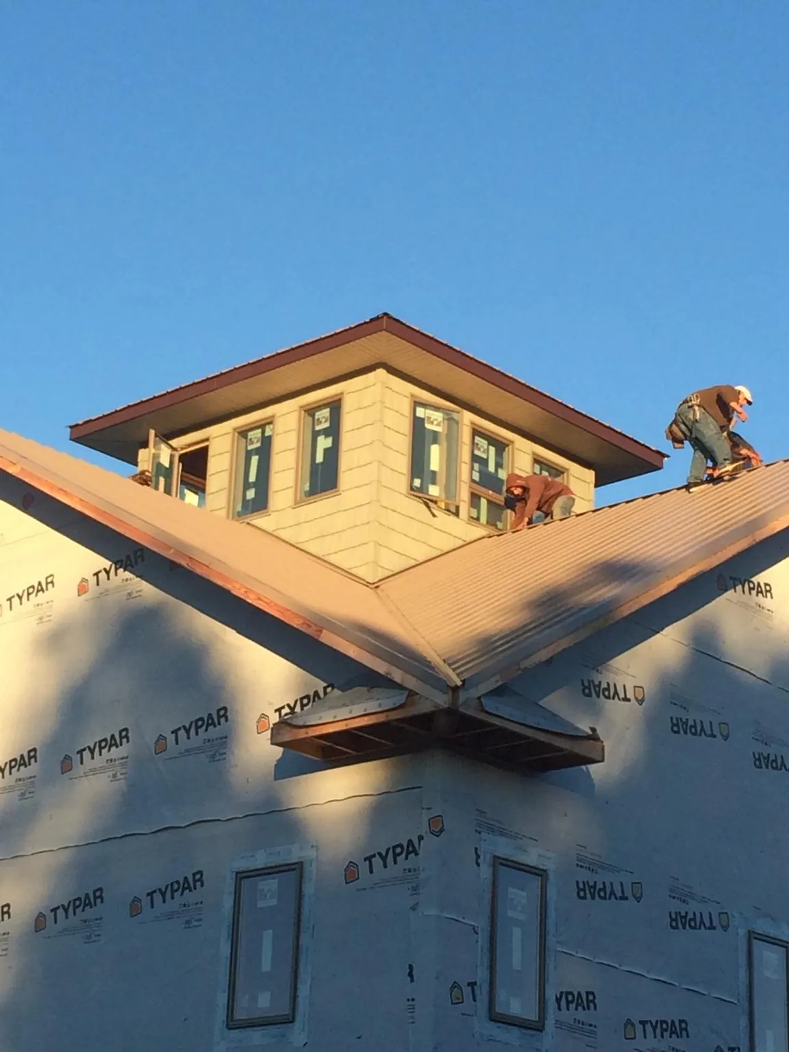 Roofers working around a rooftop cupola on a new metal roof at sunset — Roof Waterproofing in Carpenter by Roofing Brothers